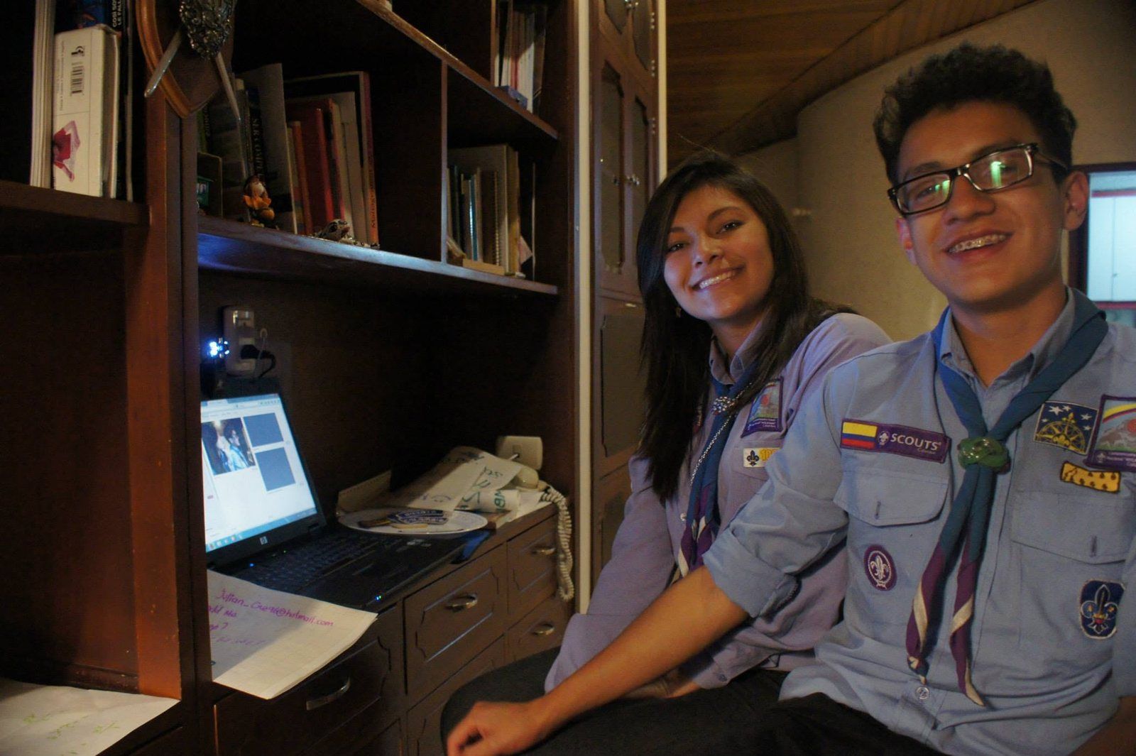 Dos scouts sonríen junto a un portátil con una videollamada abierta