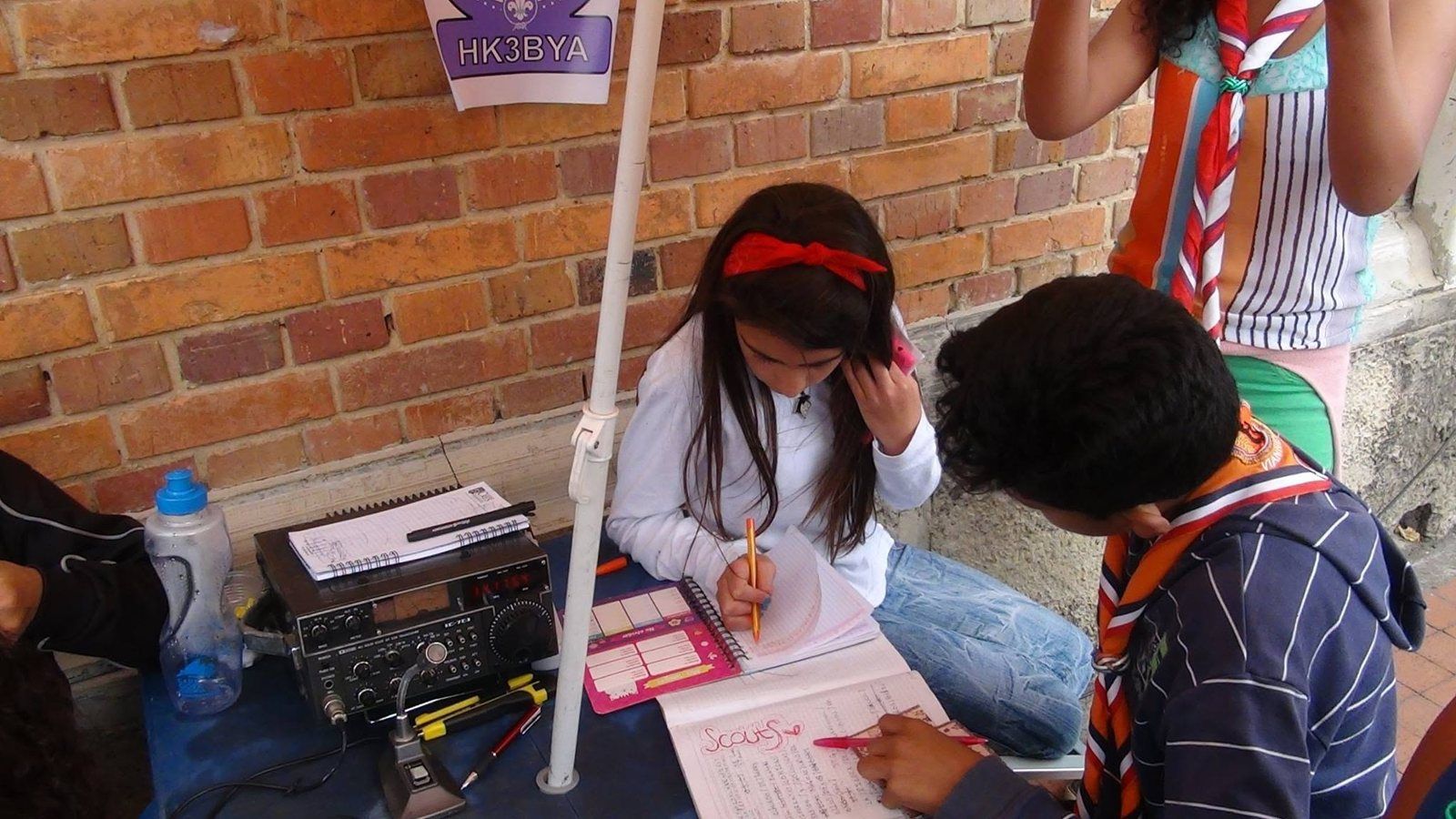 Una niña anota un contacto en la bitácora junto al radio de la estación