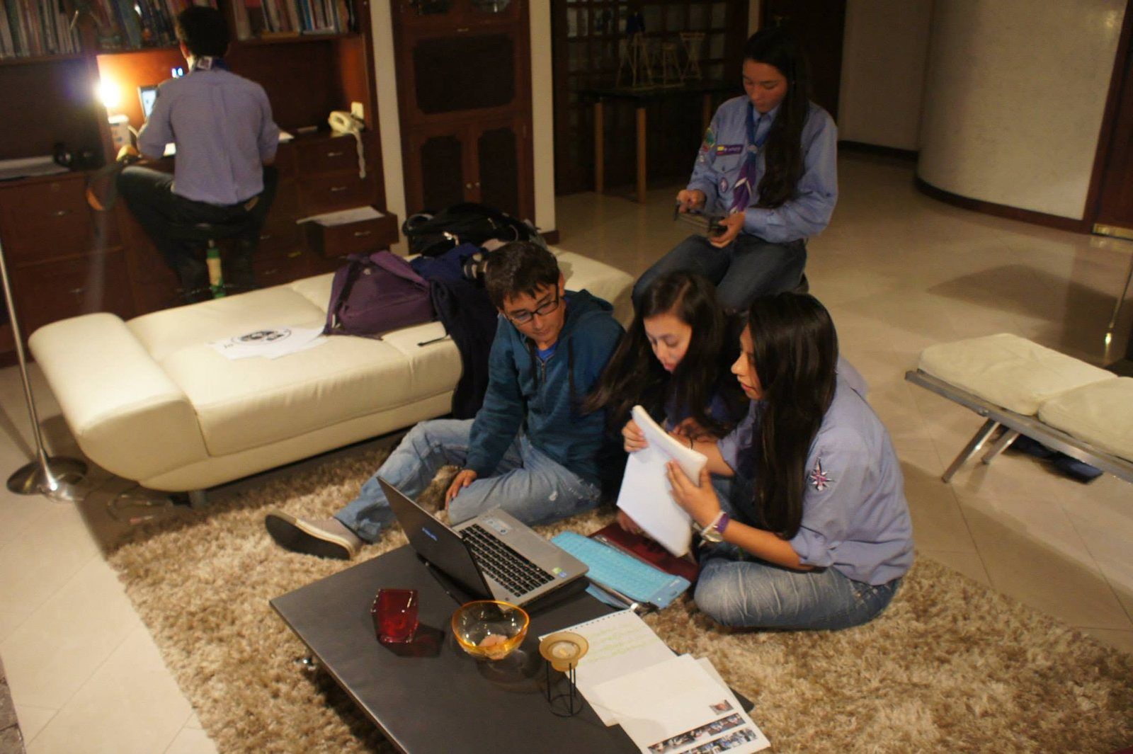 Scouts sentados en el piso resuelven una actividad con hojas y un portátil