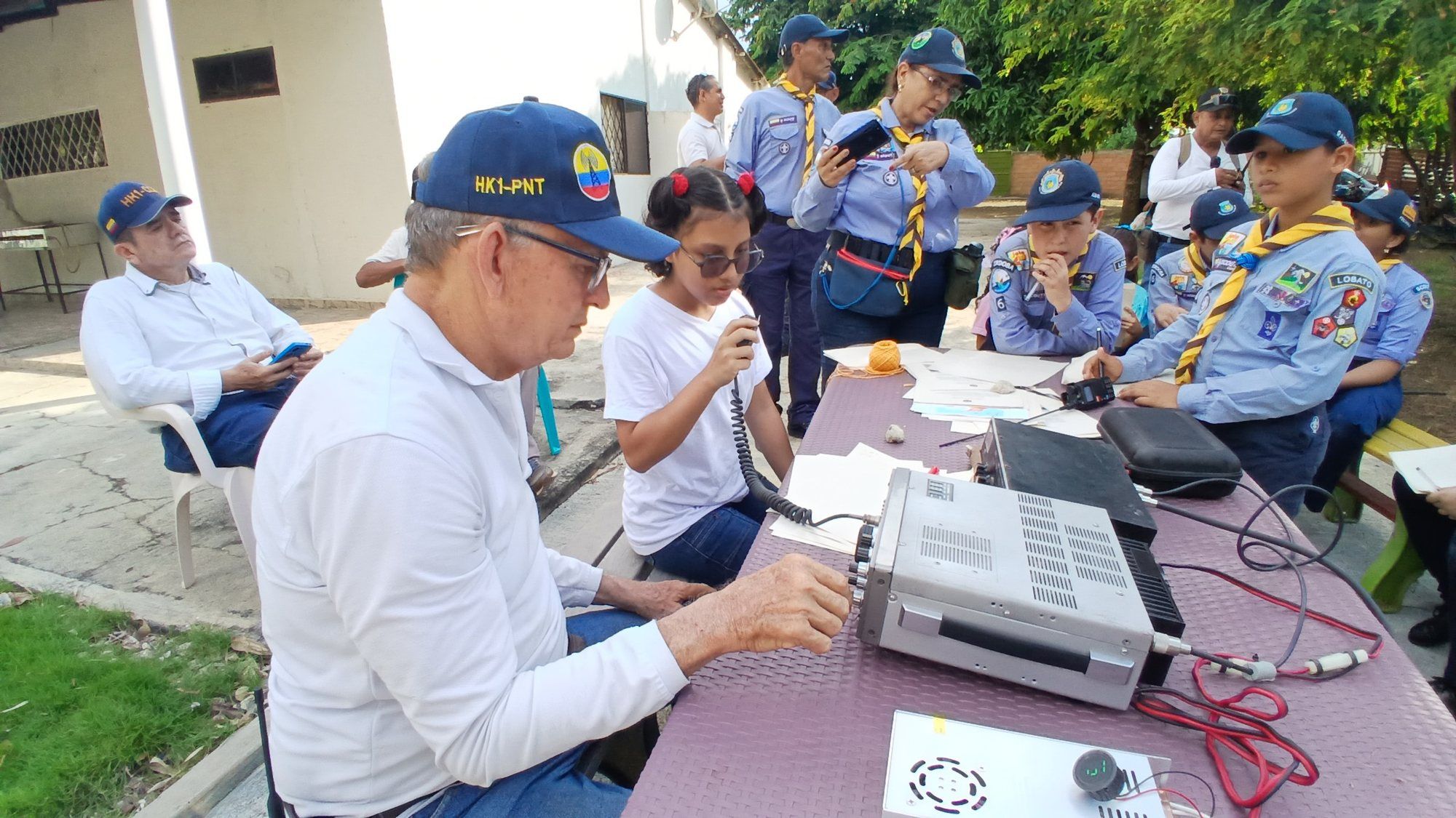 Un operador ajusta el dial mientras una niña habla al micrófono y los lobatos observan